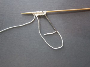 Pulling yarn tail through lower loop of furthest cast on stitch